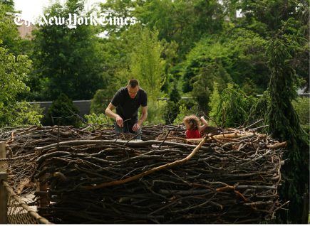 An adult and child play in a large branch nest at the Brooklyn Botanic Discovery Garden.