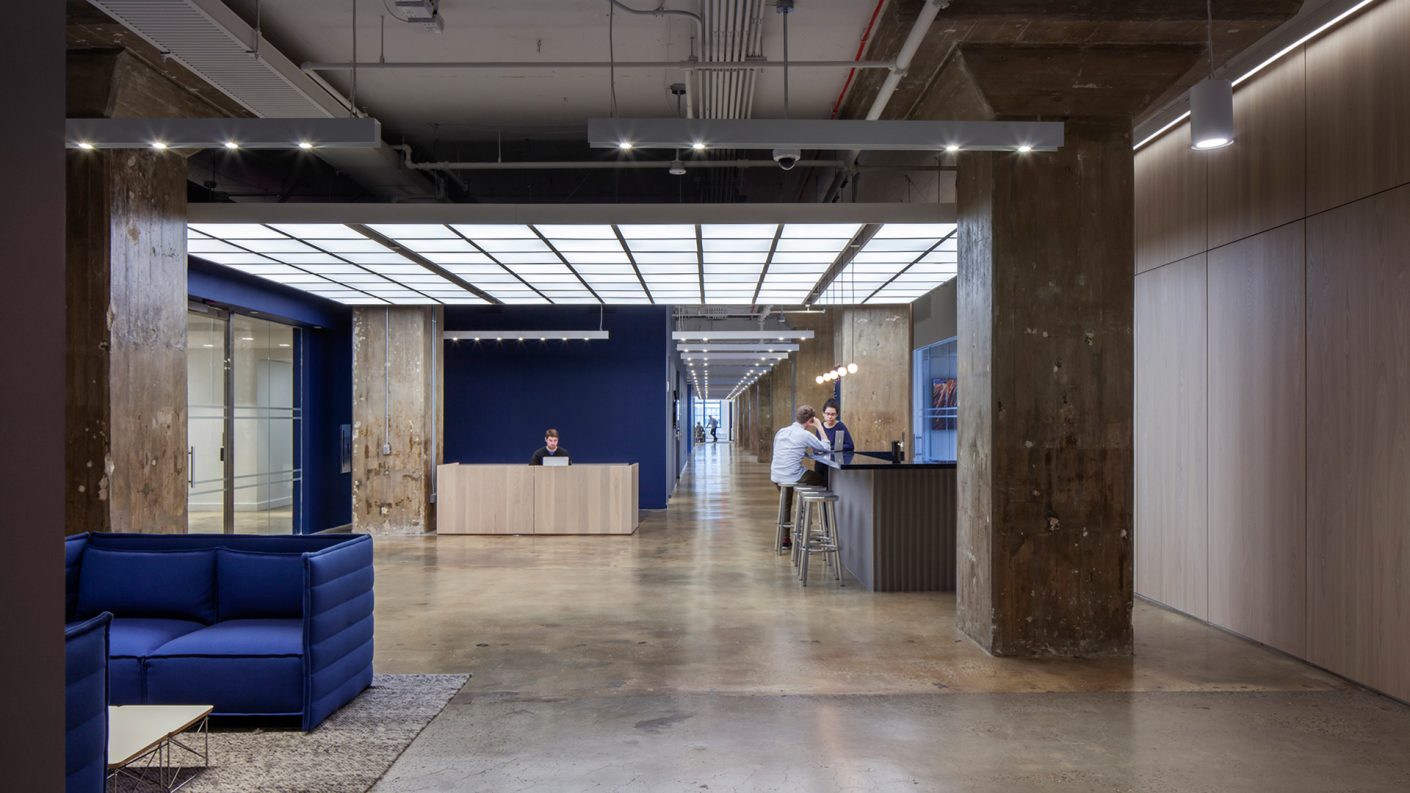 exposed concrete, an illuminated ceiling, blue sitting area and coffee bar at Harry's reception area