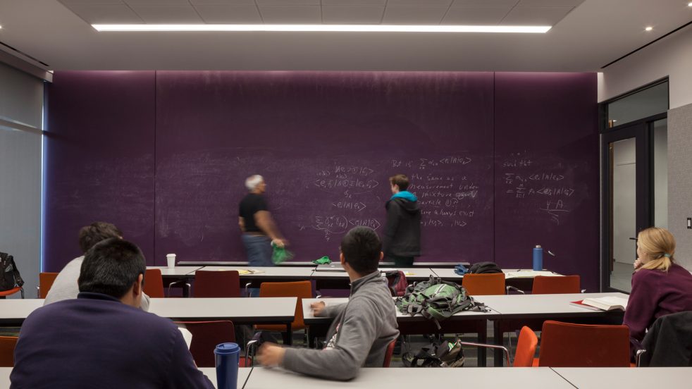 instructor and students work through math set on purple chalkboard wall