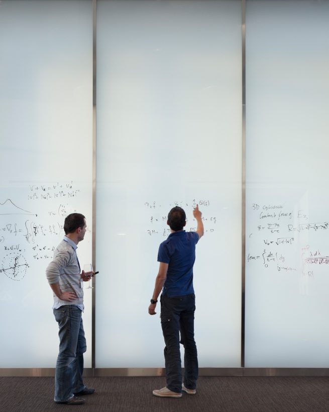 two people use writable glass panels to work on equations