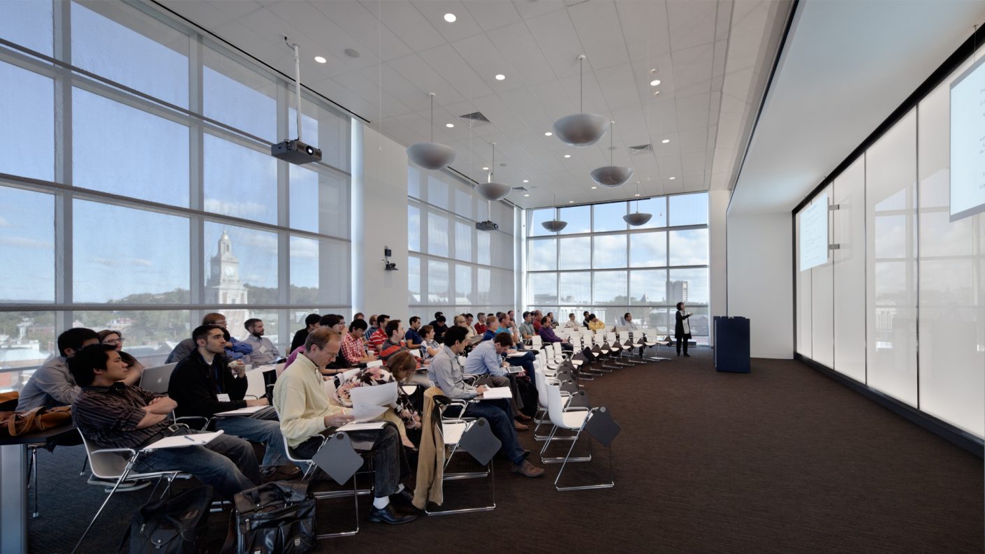 class gathered in lecture hall, facing a wall of transluscent glass and surrounded by expansive Providence views
