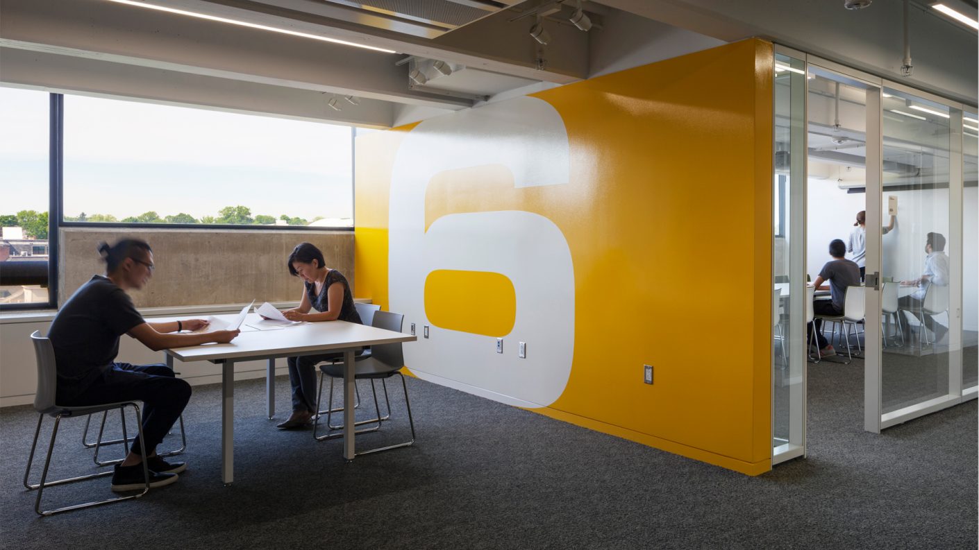 students study in open and enclosed spaces near a bright yellow wall with a large number 6 graphic