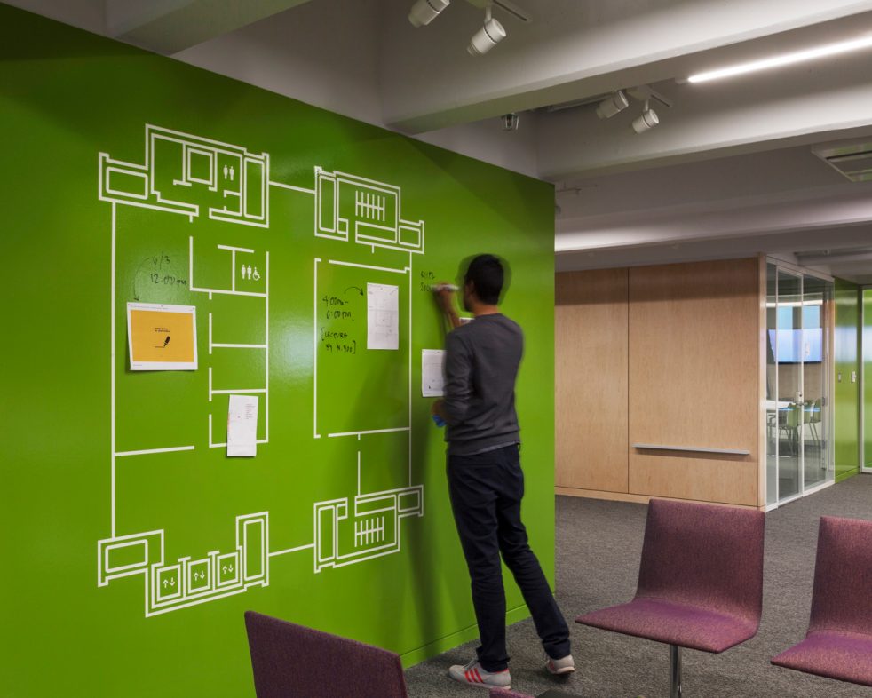 person using a bright green writable wall that includes an enlarged graphic of the floor plan