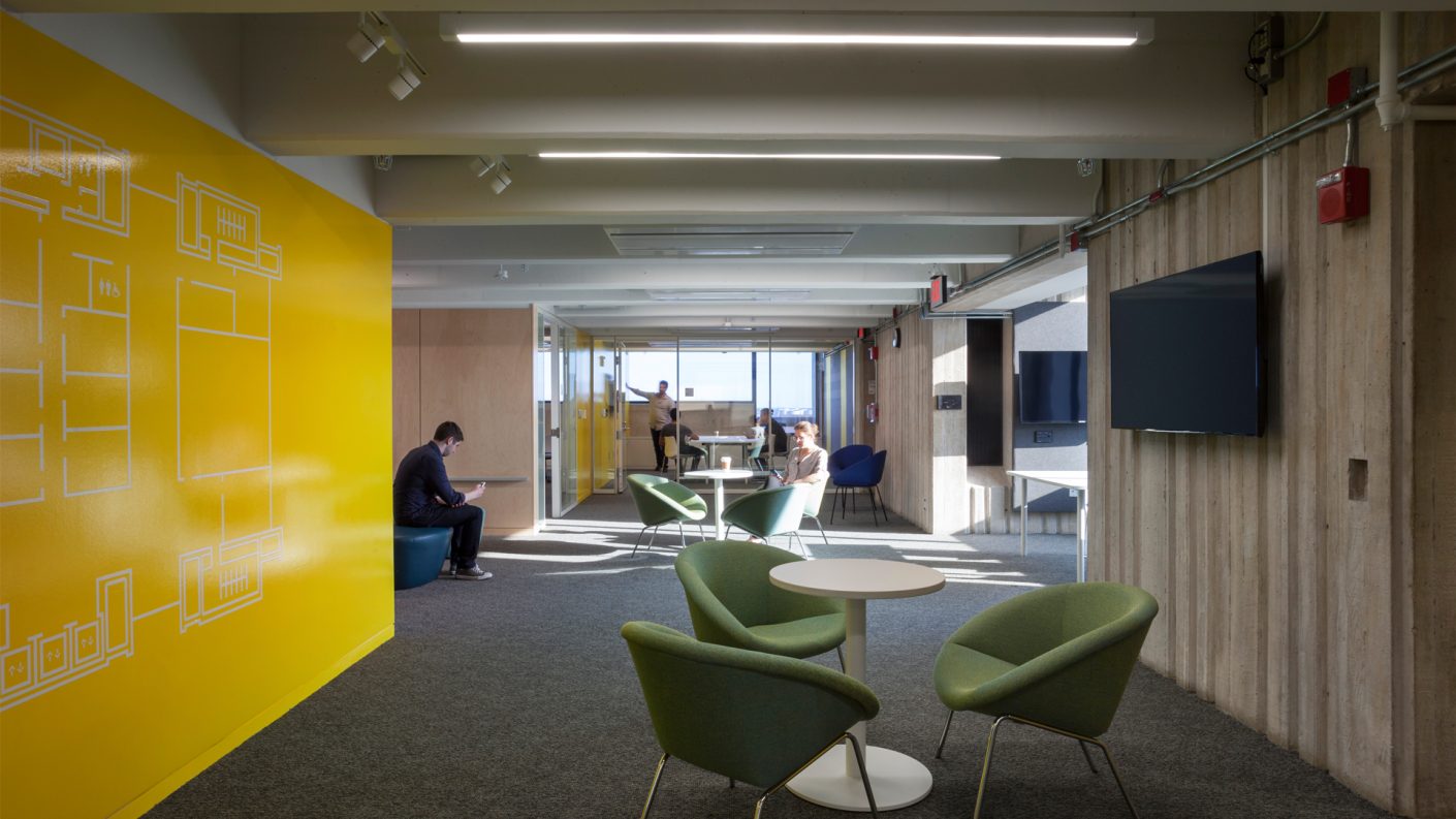 students work in common areas near a bright yellow wall and green chairs