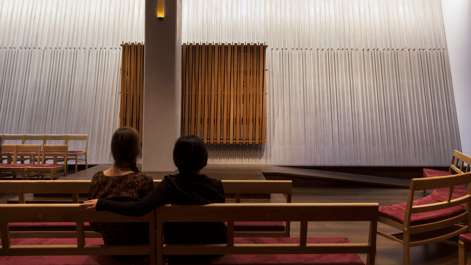 two women look upon Ark set into a canted and ribbed concrete wall
