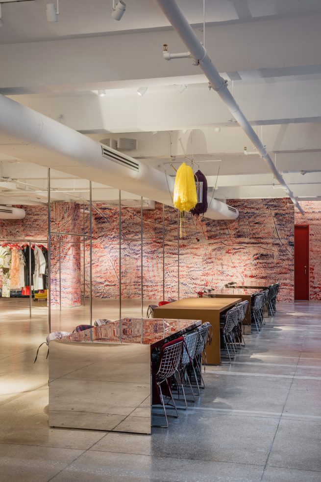 four tables inside showroom with Sterling Ruby artwork suspended above