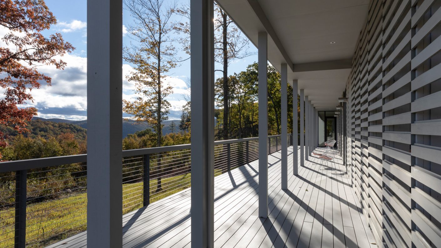 covered porch running the length of connecticut house with wood siding overlooking a valley