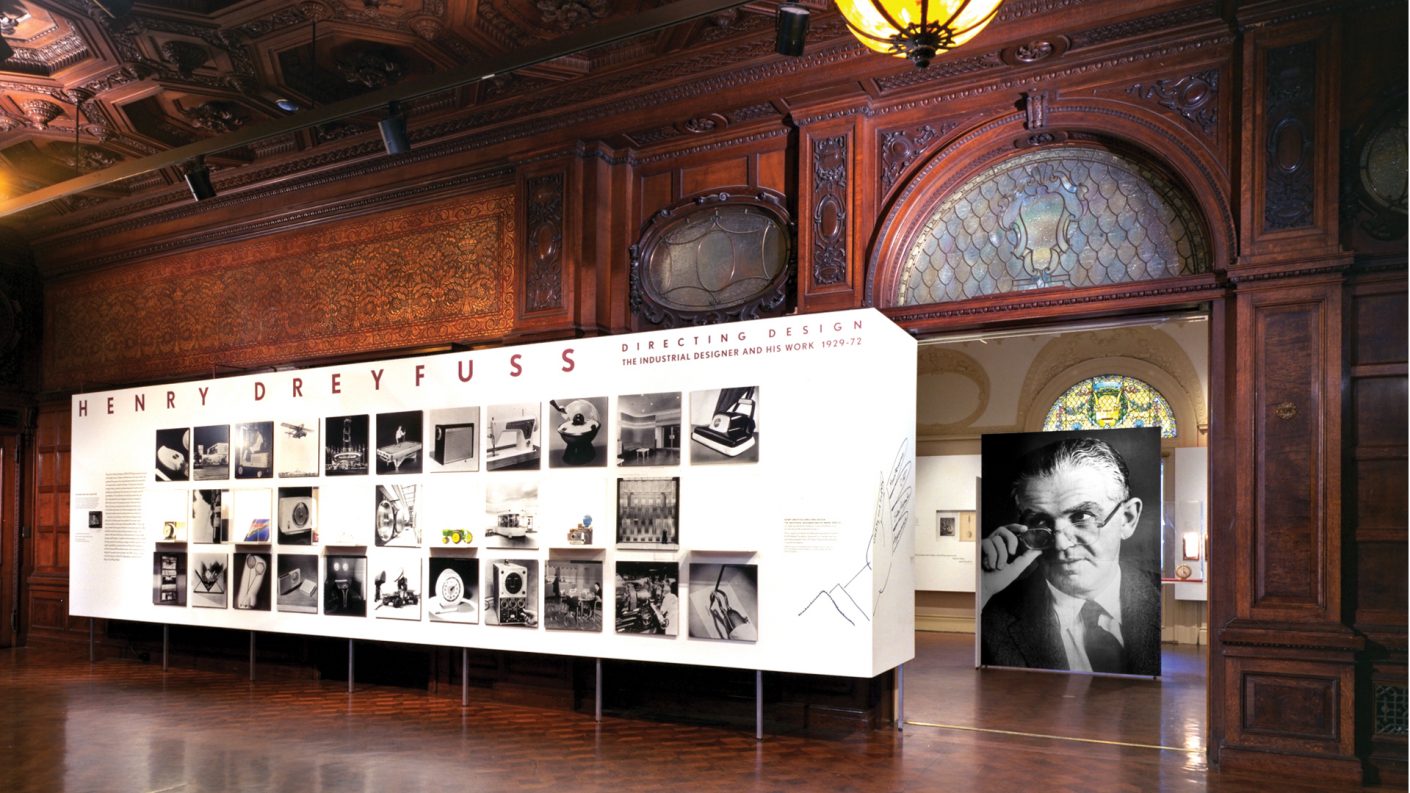 exhibition display of white wall flanked by portrait of Henry Dreyfuss