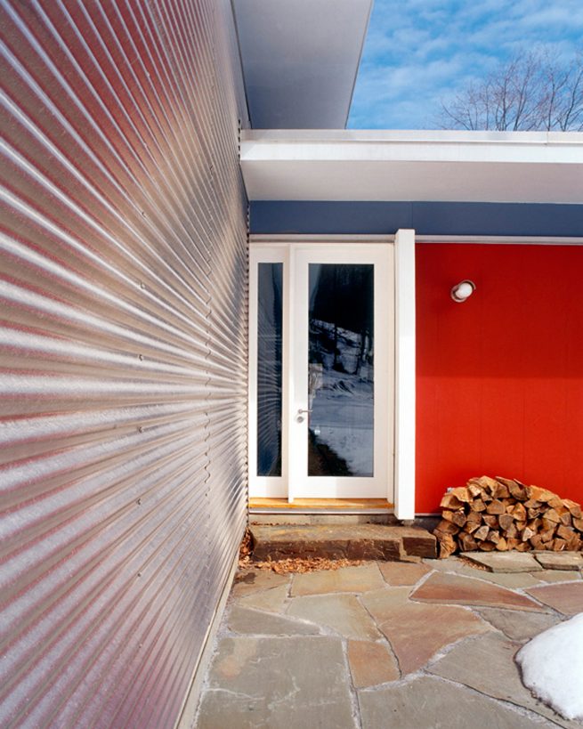 Garrison house entry in the winter framed by stacked firewood before a red wall and metal siding