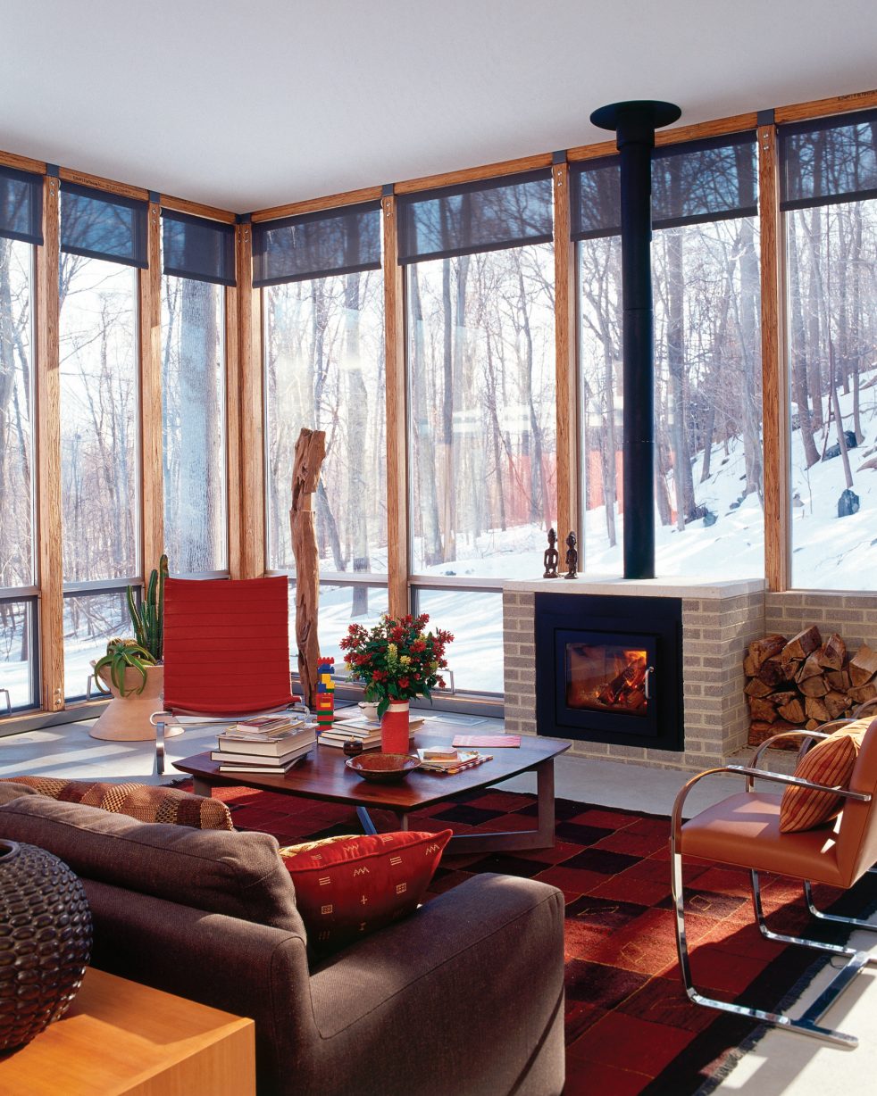 open living space with fireplace surrounded by windows and views of a snowy forest