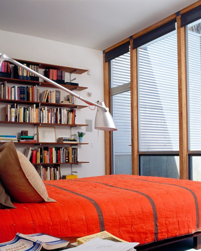 bedroom with red bed, bookshelves, and large windows