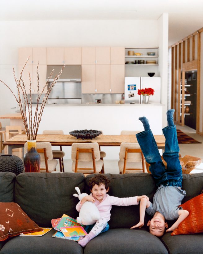 children play on couch in living area with kitchen in background