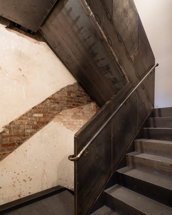 staircase landing on cellar floor reveals historic brick wall