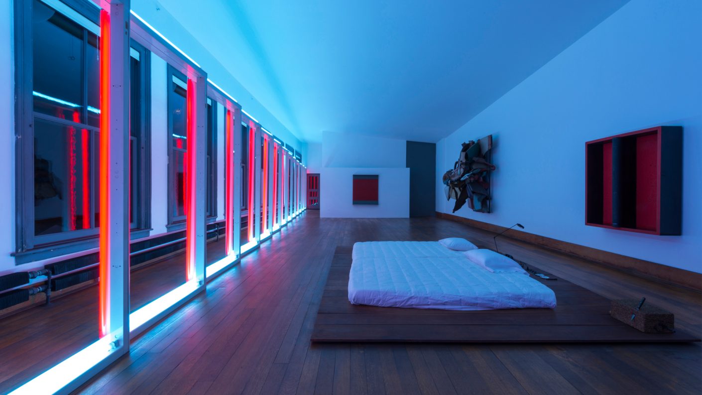 Judd's bed centered in illuminated blue and red room with works of art