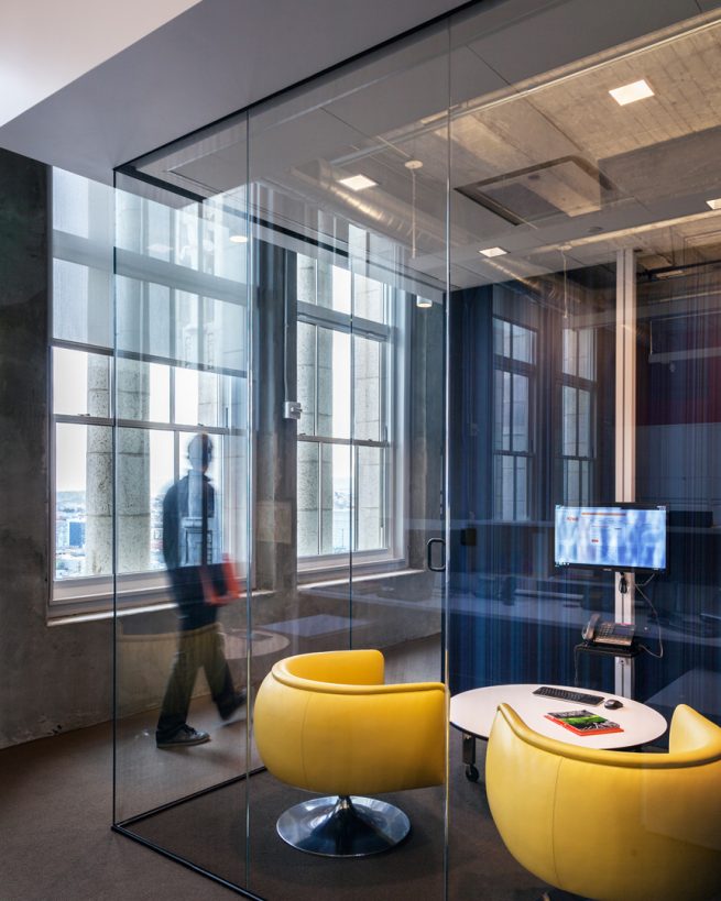 man walks past completely transparent conference room with yellow chairs