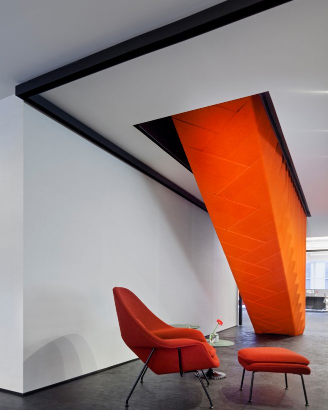 orange womb chair below a staircase wrapped in orange felt