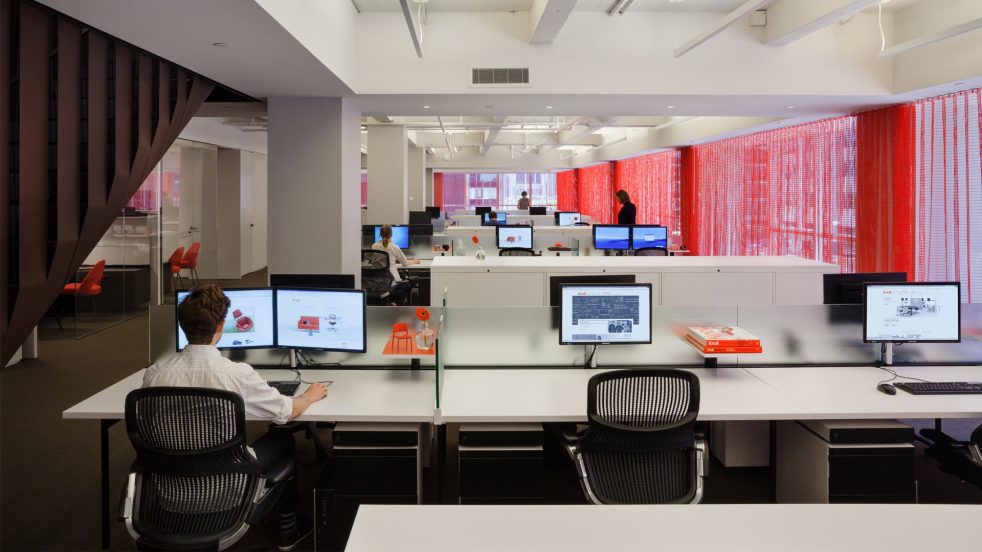 man works at his desk next to leather wrapped staircase in an open office plan lined with red curtains