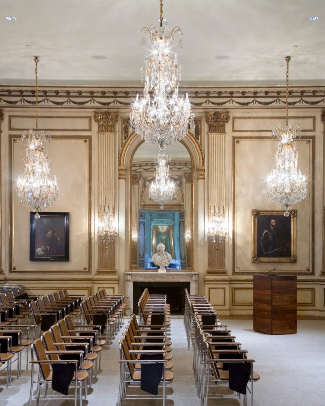 music room lecture hall with ornate chandeliers and aligned chairs