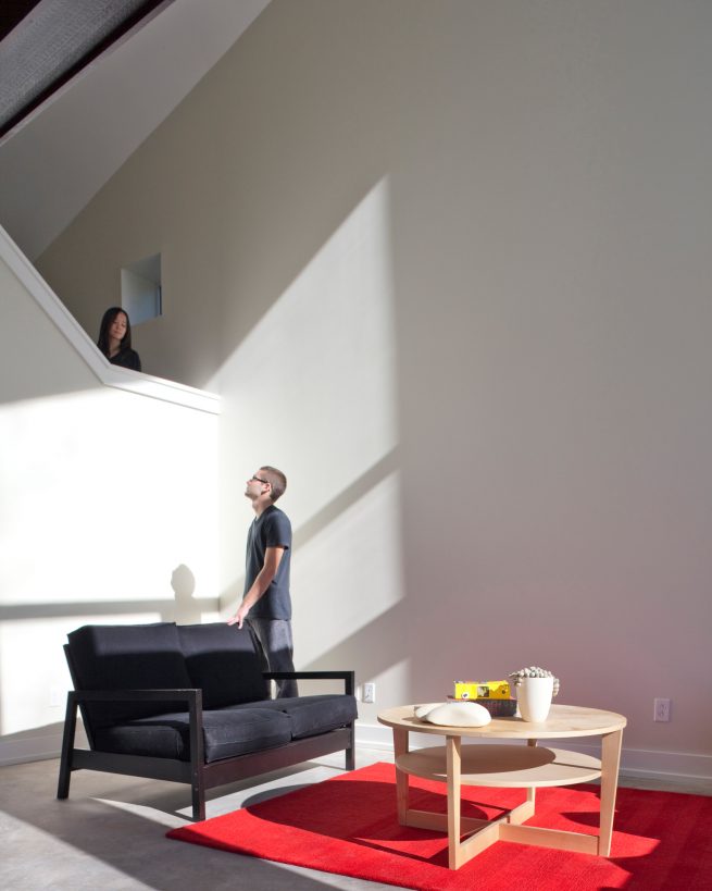 a man looks up at a woman on a stair landing that's open to a bright living space