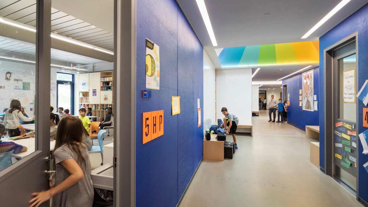 student enters classroom, while others occupy blue sawtooth hallway