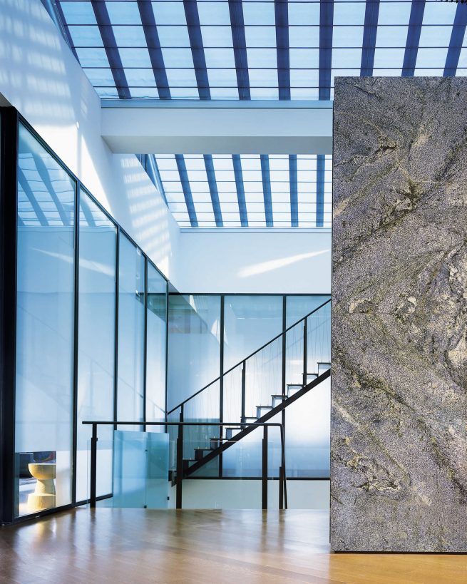 staircase reveals itself from behind large granite wall under glass ceiling