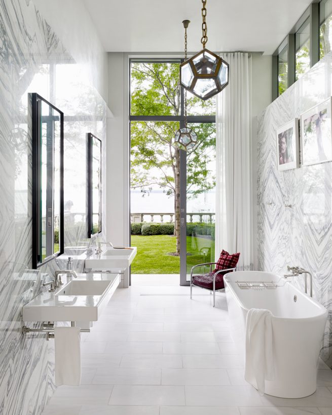 white marble bathroom leading out to lawn and lake