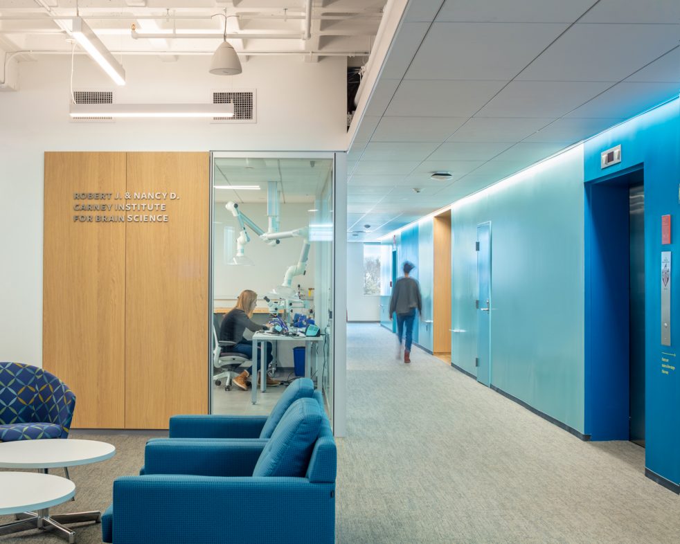 Student researcher at Carney Institute lab and person walking down a blue-walled hall