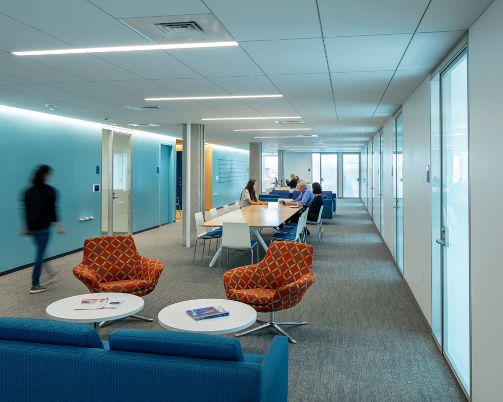 People meeting and walking through a long open study area between a bright blue wall and translucent offices