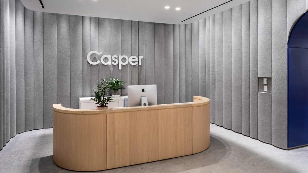 Wooden reception desk with plant and computer surrounded by grey felt walls with Casper logo