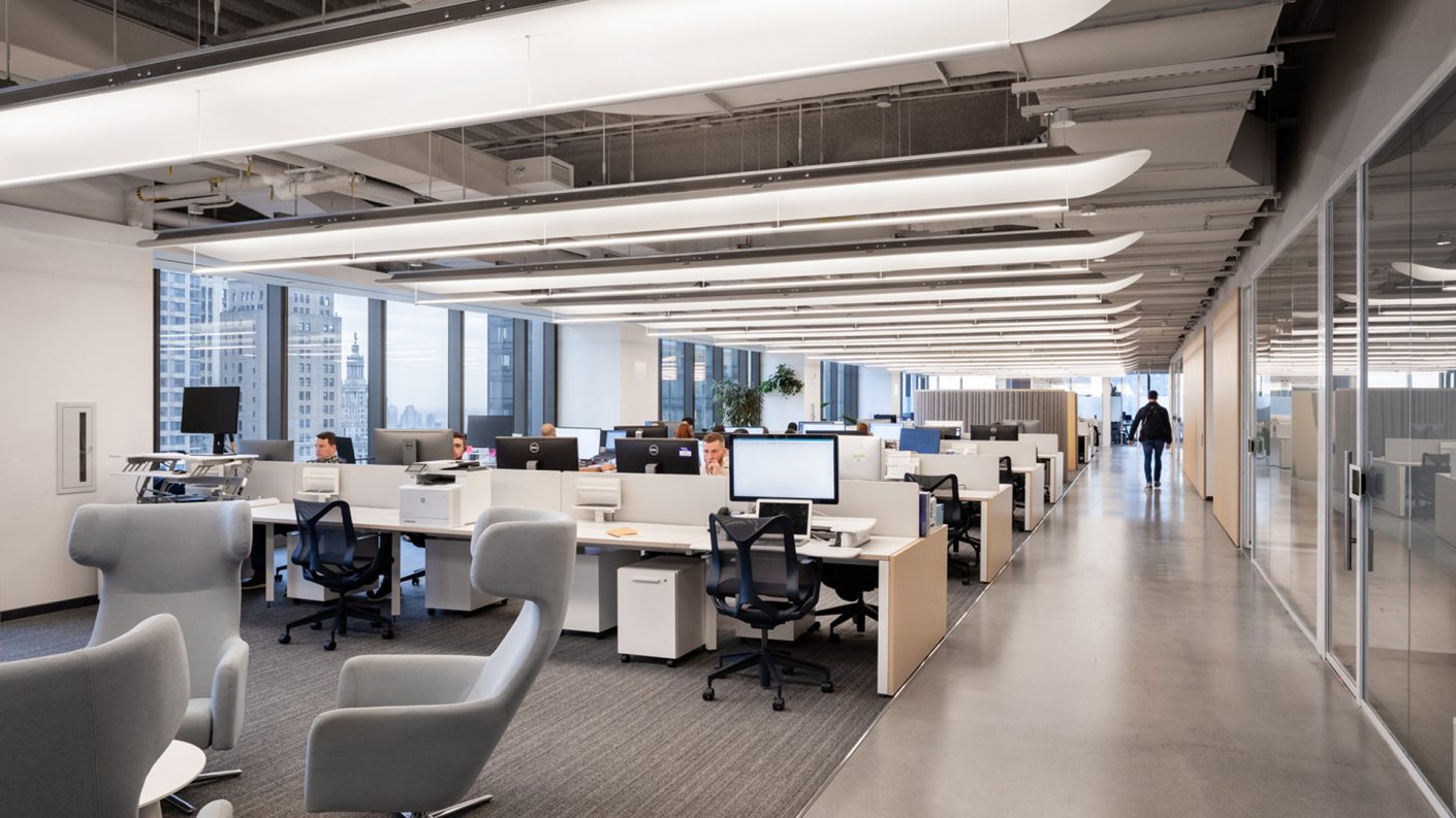 Long open office layout with curved light baffles above and glass doors on the right