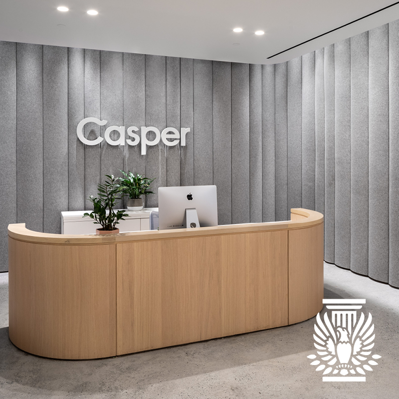 Wooden reception desk with plant and computer surrounded by grey felt walls with Casper logo