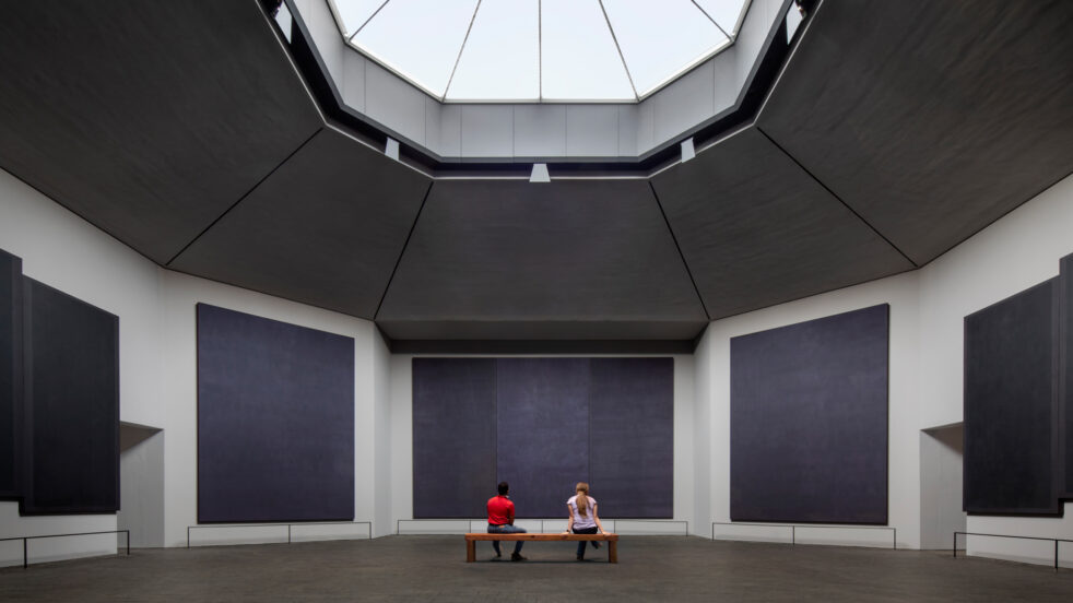 Photograph of two people sitting on a bench in front of Mark Rothko paintings