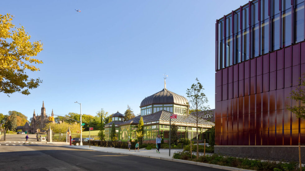 View of historic greenhouse with burgundy terra cotta-clad visitor's center in foreground and brownstone cemetery gates in background. Image Credit: Rafael Gamo