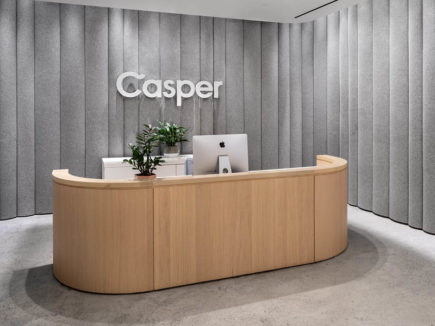 Wooden reception desk with plant and computer surrounded by grey felt walls with Casper logo