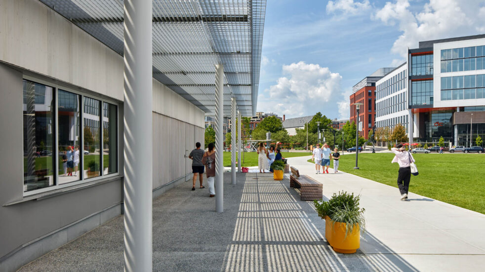 People walk by a shaded pavilion in a city park.