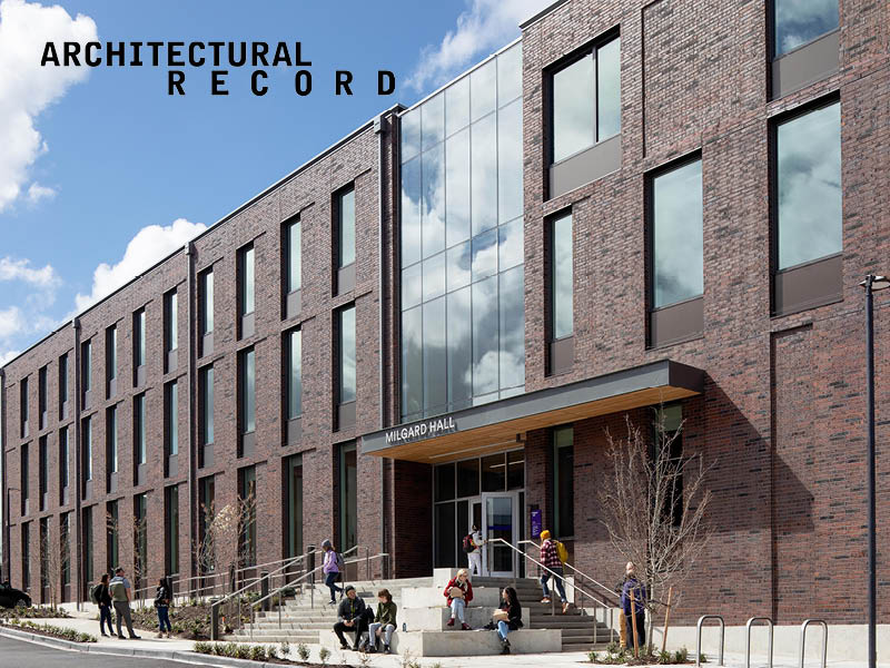 Photo of people walking in and out of a 3-story brick building, and sitting on entry steps