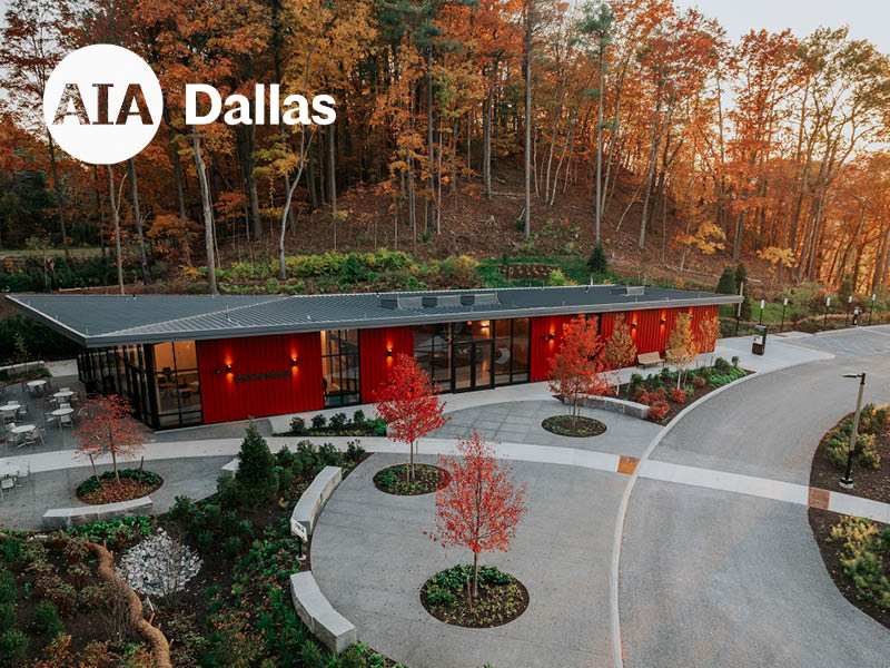 Red, one-story building with woods in the background and planted landscape in the foreground.