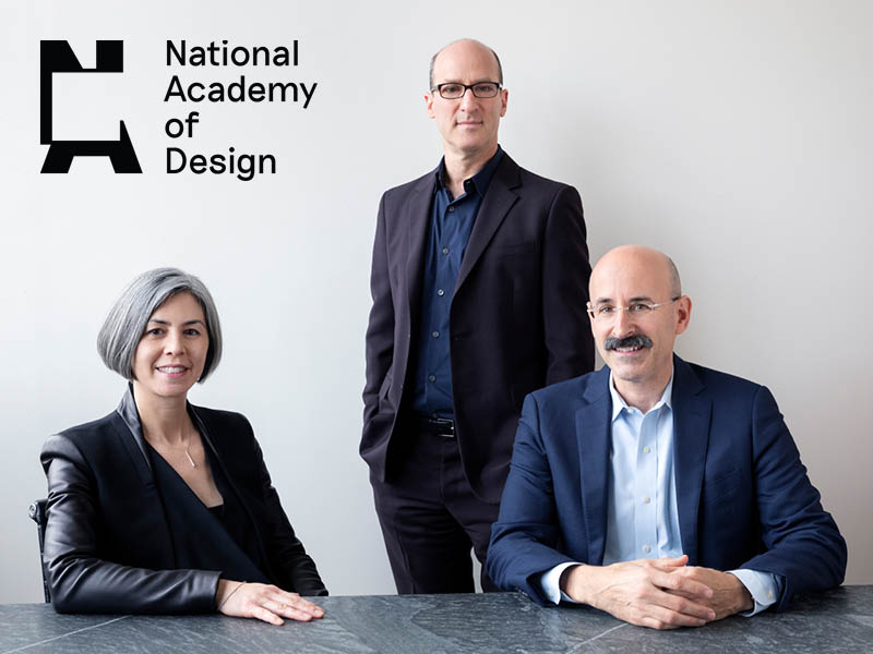 A woman and two men sit and stand in front of a white background