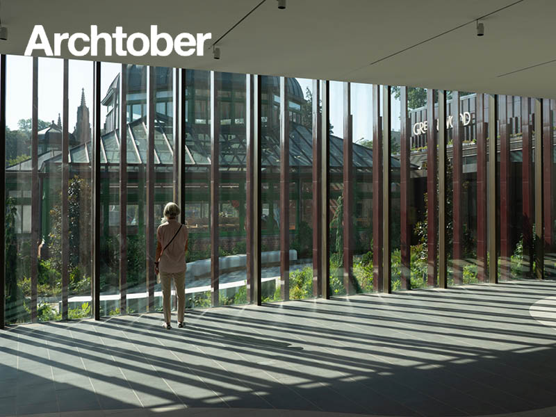 Woman stands in front of large window looking out to a greenhouse.