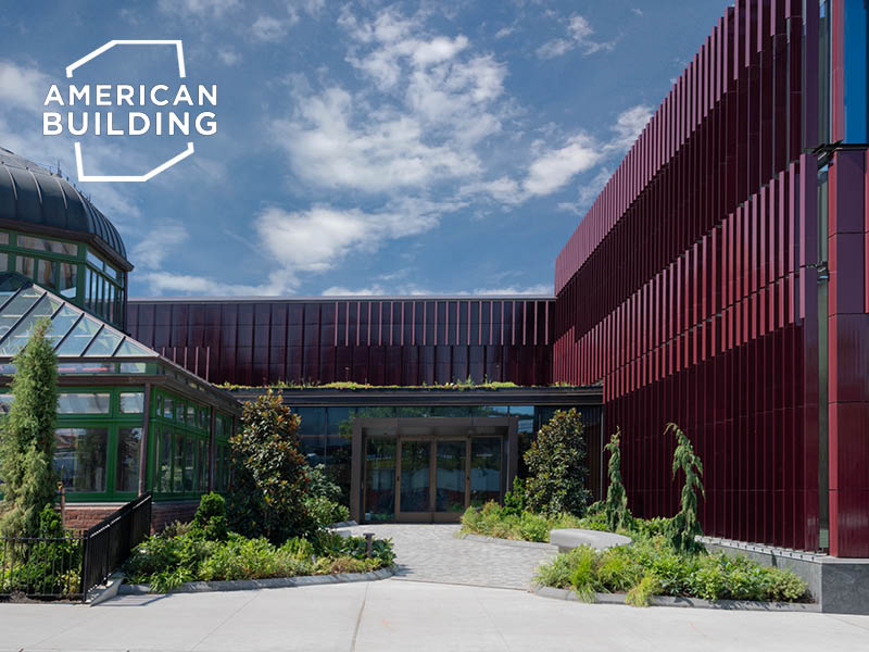 Planted entry court in front of a terra cotta building and a historic greenhouse.