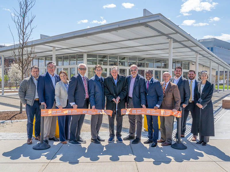 group of people cuts an orange ribbon in front a metal pavilion