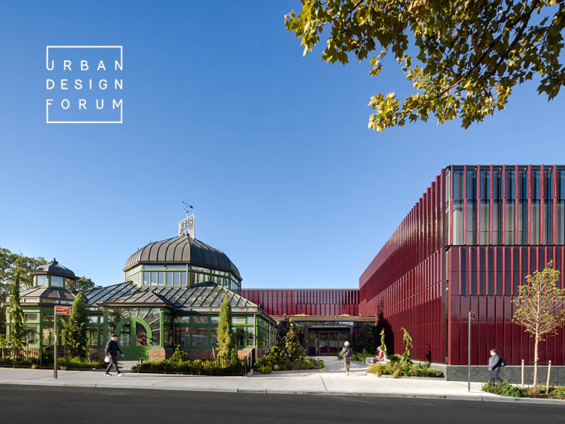 People walking towards a historic greenhouse and a new burgundy terra cotta-clad visitors center.