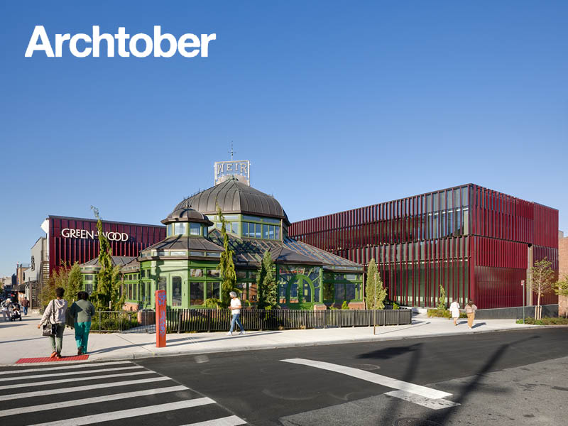 People walk in front of a restored historic greenhouse and burgundy terra cotta-clad visitor's center.