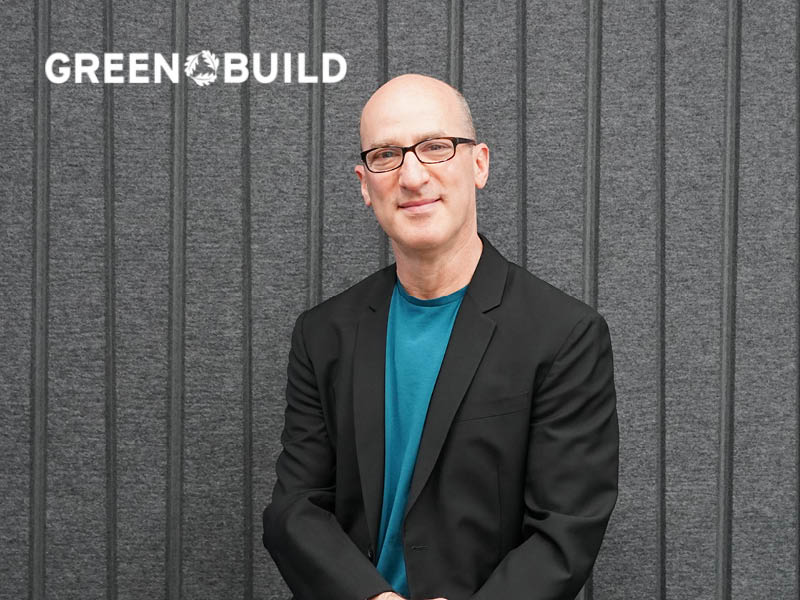 A man in blue shirt sits in front of a gray background